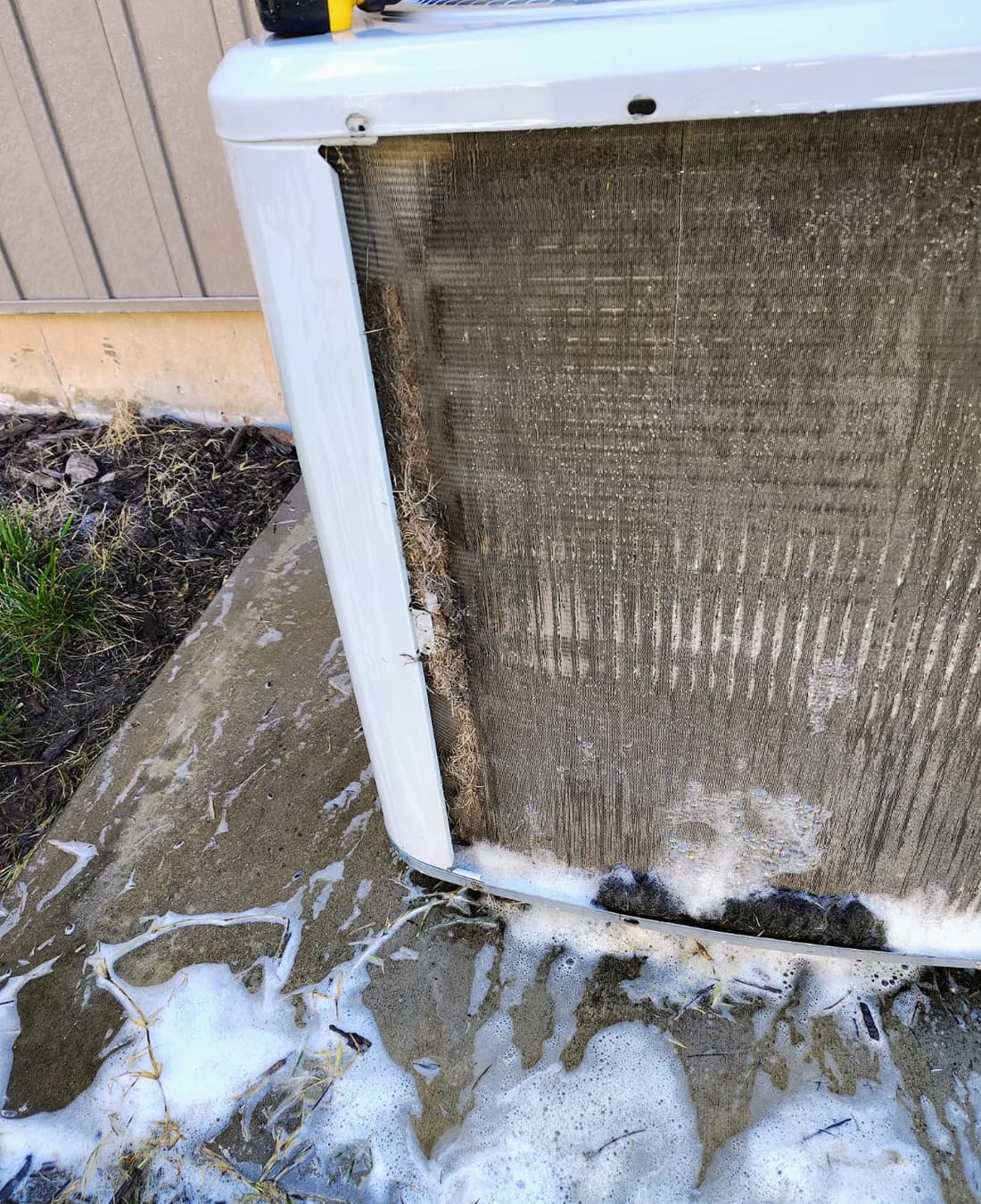 Foam and debris on an exposed outdoor condenser coil during cleaning