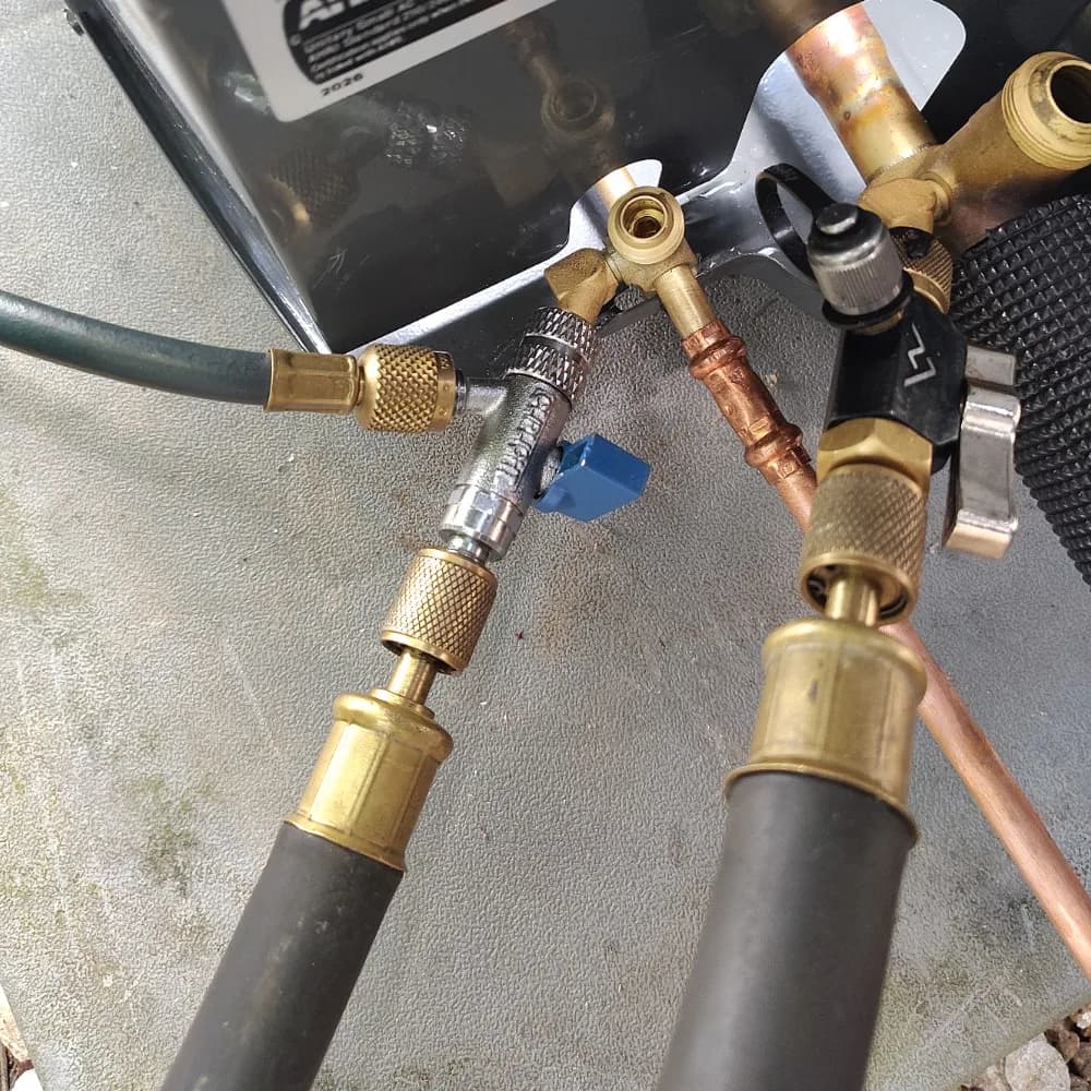 HVAC service hoses and valve tools connected at an outdoor air conditioner service port
